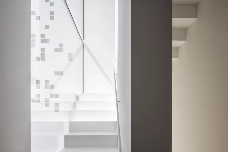 White floating staircase with metal handrail beside a wall with scattered square grey tiles