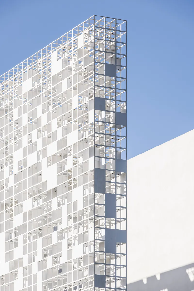 Corner view of the pixelated glass and white panel facade against a clear blue sky