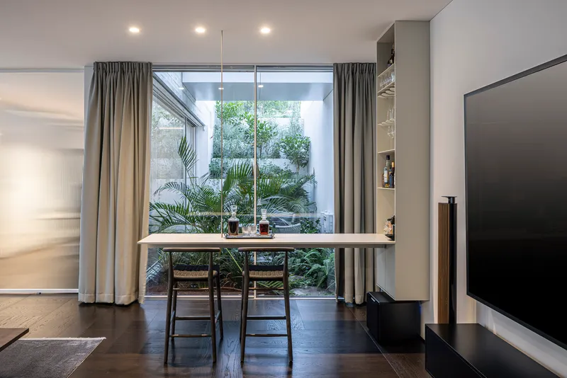 Dining area with two chairs facing a glazed courtyard filled with potted palms and greenery