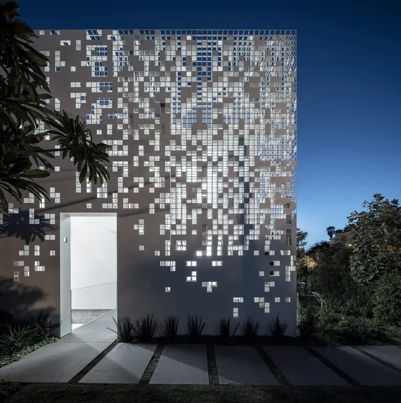 Street entrance with paved walkway and planted beds leading to the pixelated facade at twilight