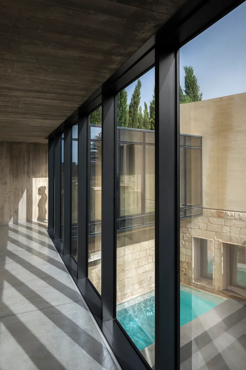 Corridor with black steel windows framing views of stone facade and pool below
