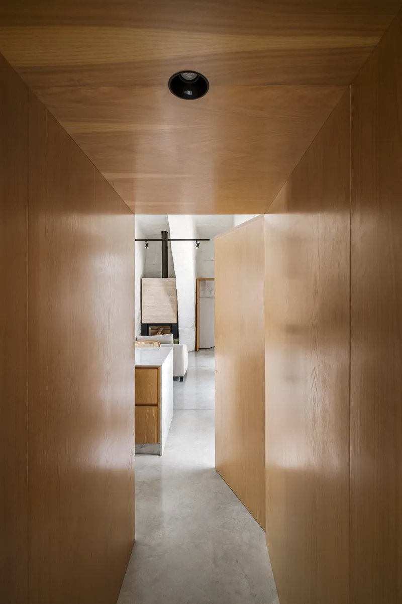Timber-clad corridor with backlit translucent panels leading toward bathroom at the end
