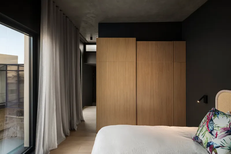 Bedroom with oak wardrobe panels, grey curtains and exposed concrete ceiling