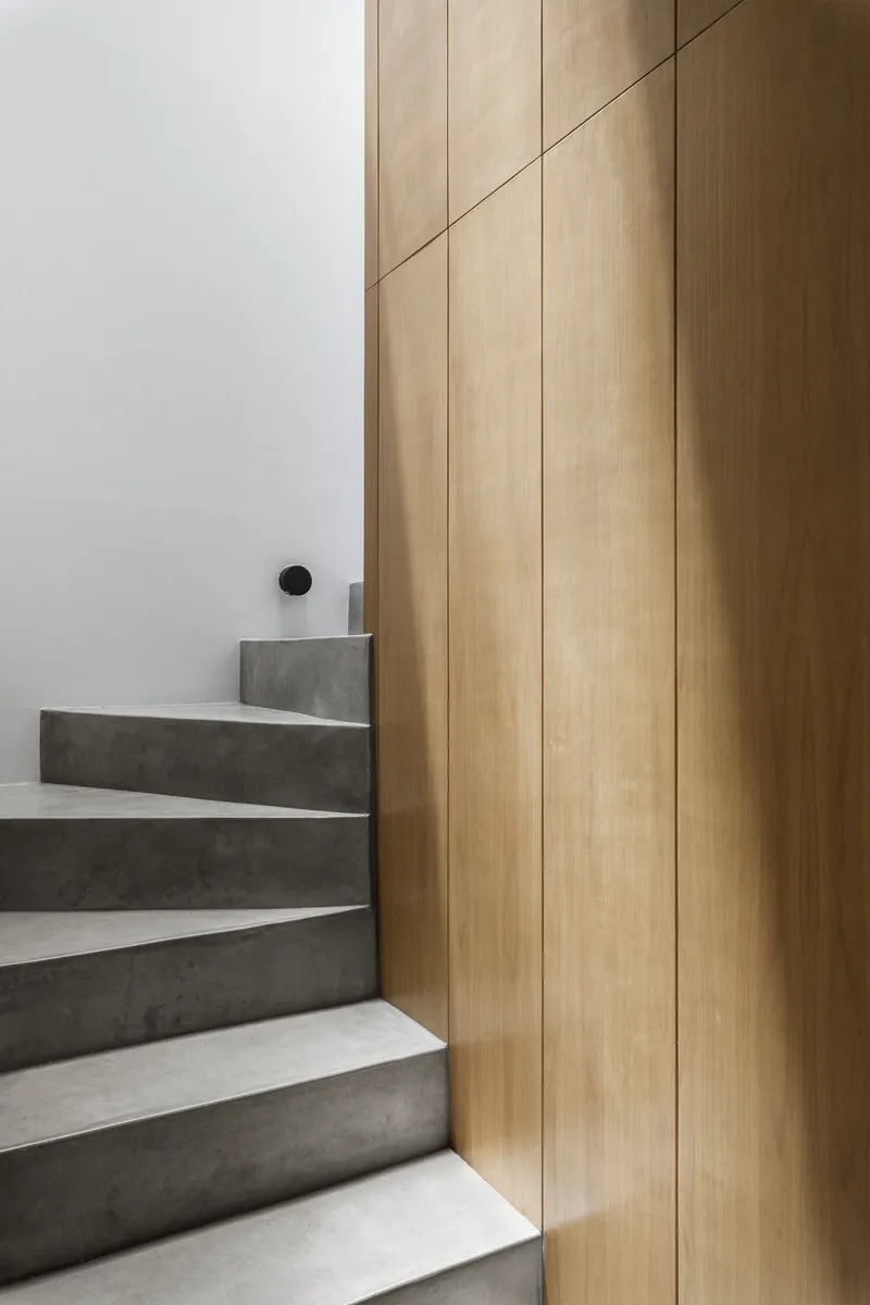Concrete staircase with white risers meeting a vertical oak paneled wall