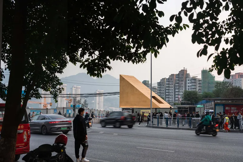 Cantilevered timber volume framed by tree branches with traffic and pedestrians crossing the street below