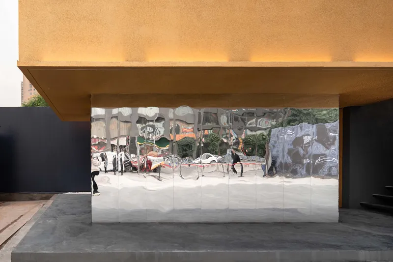 Covered entrance with reflective mirrored wall beneath a cantilevered overhang and pedestrian visible in reflection