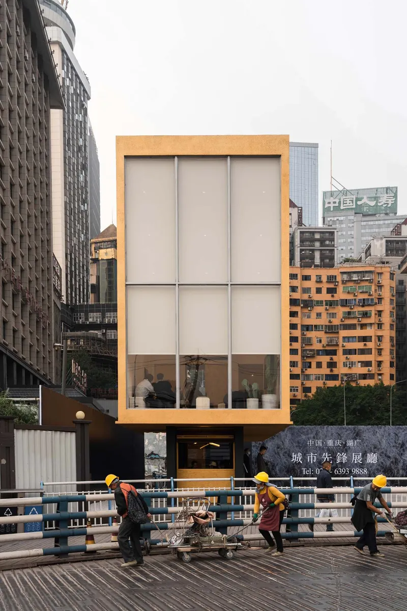 Cantilevered pavilion with yellow frame and translucent panels overlooking workers on the roadway