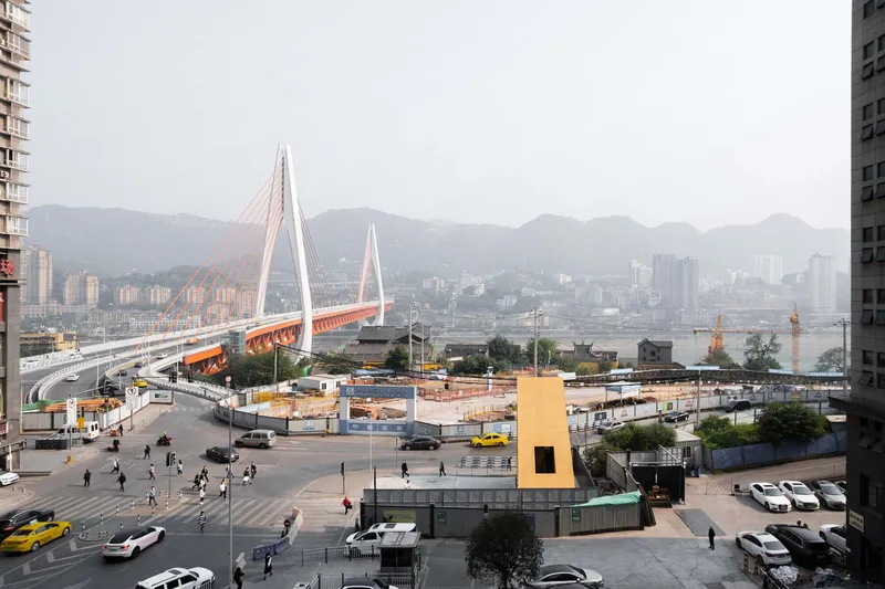 Yellow kiosk structure in foreground with cable-stayed bridge and mountains visible beyond