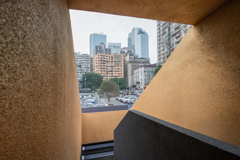 Triangular window opening framing the urban skyline beyond the textured ochre interior walls