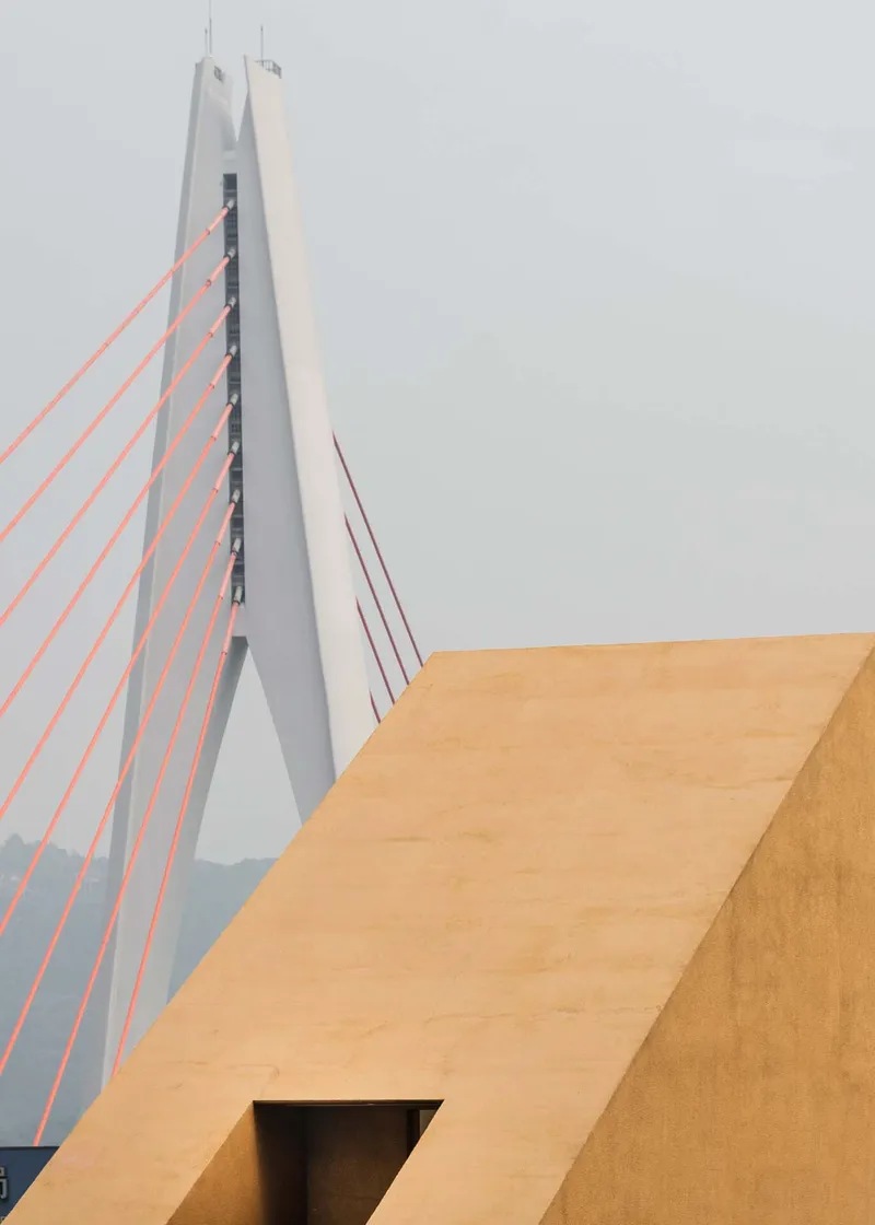 Angular ochre volume with rectangular aperture against the white pylon of a cable-stayed bridge