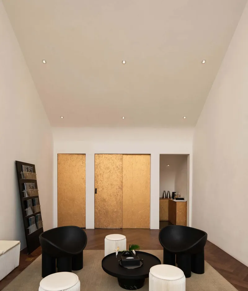 White interior room with cork-clad sliding doors and recessed ceiling spotlights above dark seating