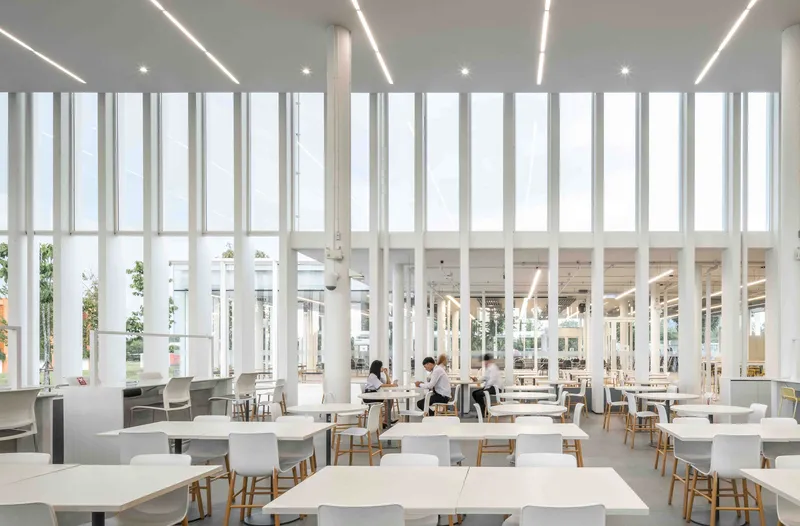 Interior dining hall with vertical white mullions filtering daylight and two students seated at tables
