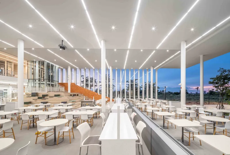 Dining hall interior showing timber stair, vertical louvers, and rows of tables beneath linear lighting