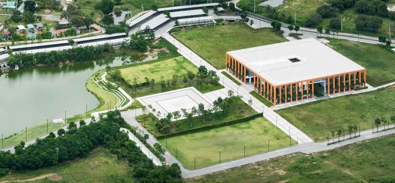 Aerial view of the complex with vertical timber facade, green roofs, and adjacent pond