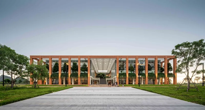 Front elevation of the timber-framed colonnade and glass facade across a paved plaza at dusk