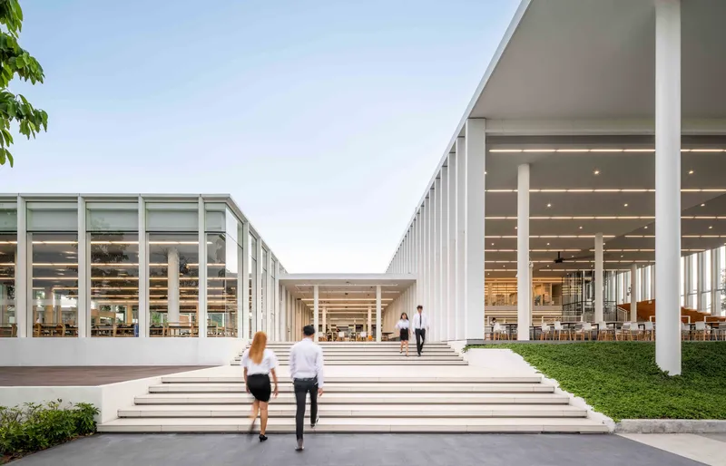 Wide stepped entry plaza with two figures ascending toward the recessed glazed volumes