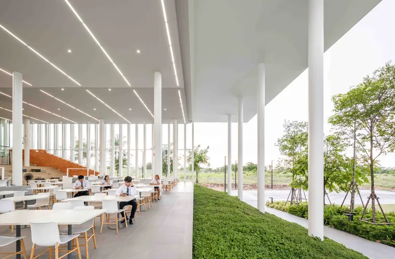 Canteen interior with white columns and linear ceiling lights opening to landscaped perimeter