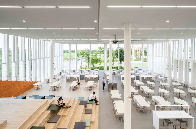 Dining hall with tiered timber seating and vertical fin curtain walls under recessed lighting