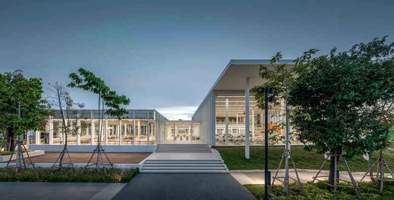 Front entry approach with wide steps leading to a glazed pavilion framed by young trees at dusk