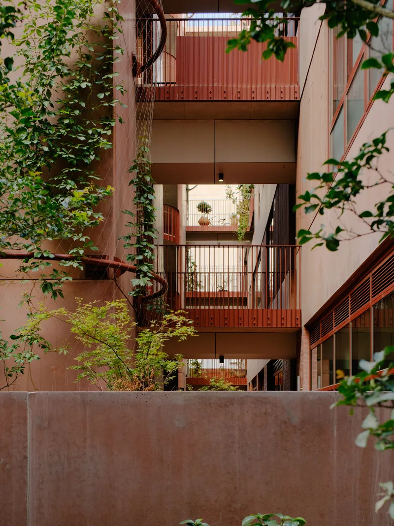 View across the courtyard showing stacked balconies with metal railings framed by climbing vines