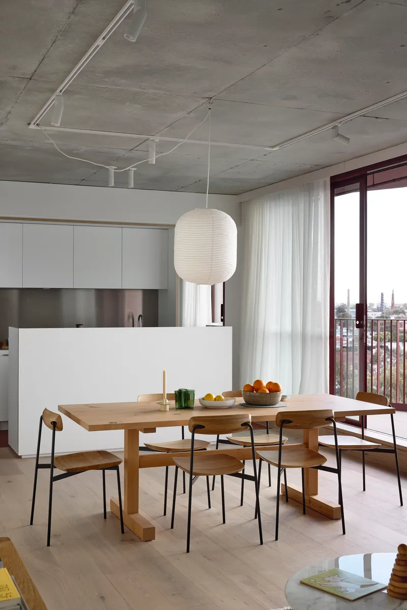 Open kitchen and dining area with exposed concrete ceiling and sheer curtains at the balcony door