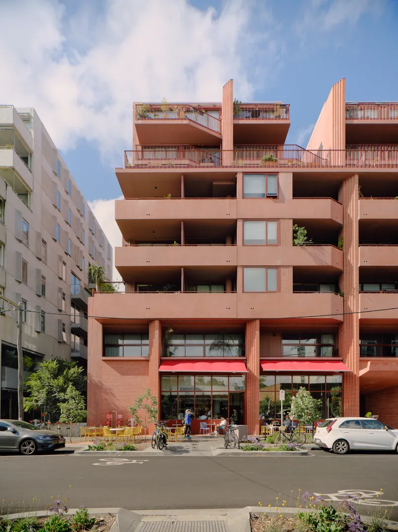 Ground floor cafe with red awning and yellow outdoor furniture below residential terraces