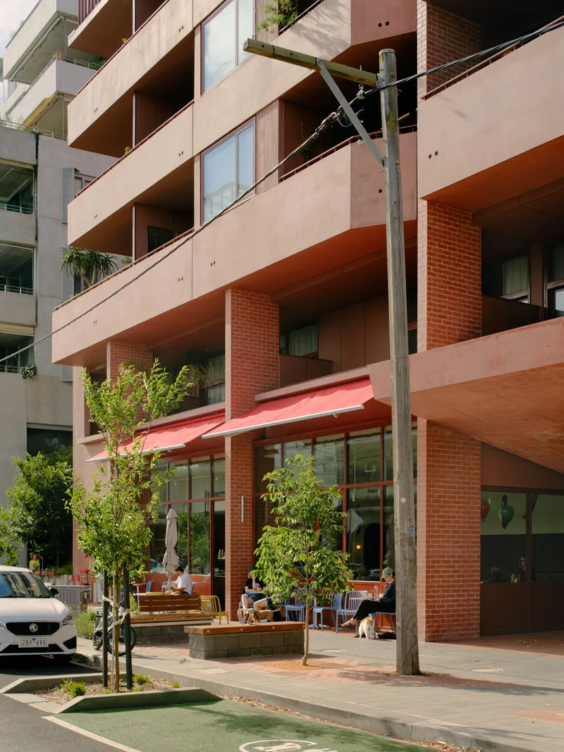 Street-level entrance colonnade with red brick columns framing cafe seating and planted beds