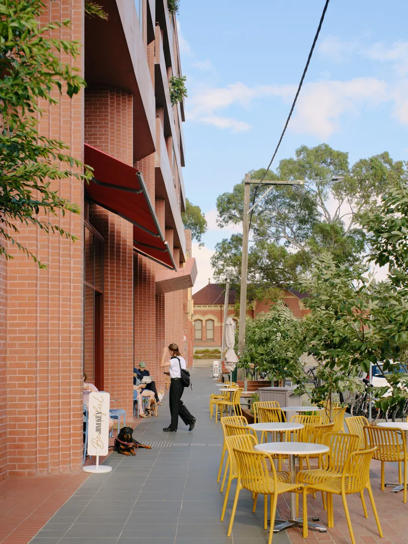 Outdoor terrace with yellow chairs and planted beds along red brick colonnade