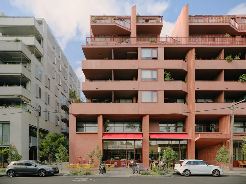 Street view of the terracotta brick facade with deep recessed balconies and ground floor cafe