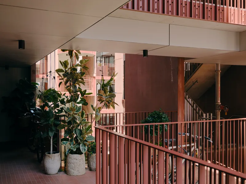 Interior walkway with pink vertical slat railings and potted plants under white ceilings with angular beams