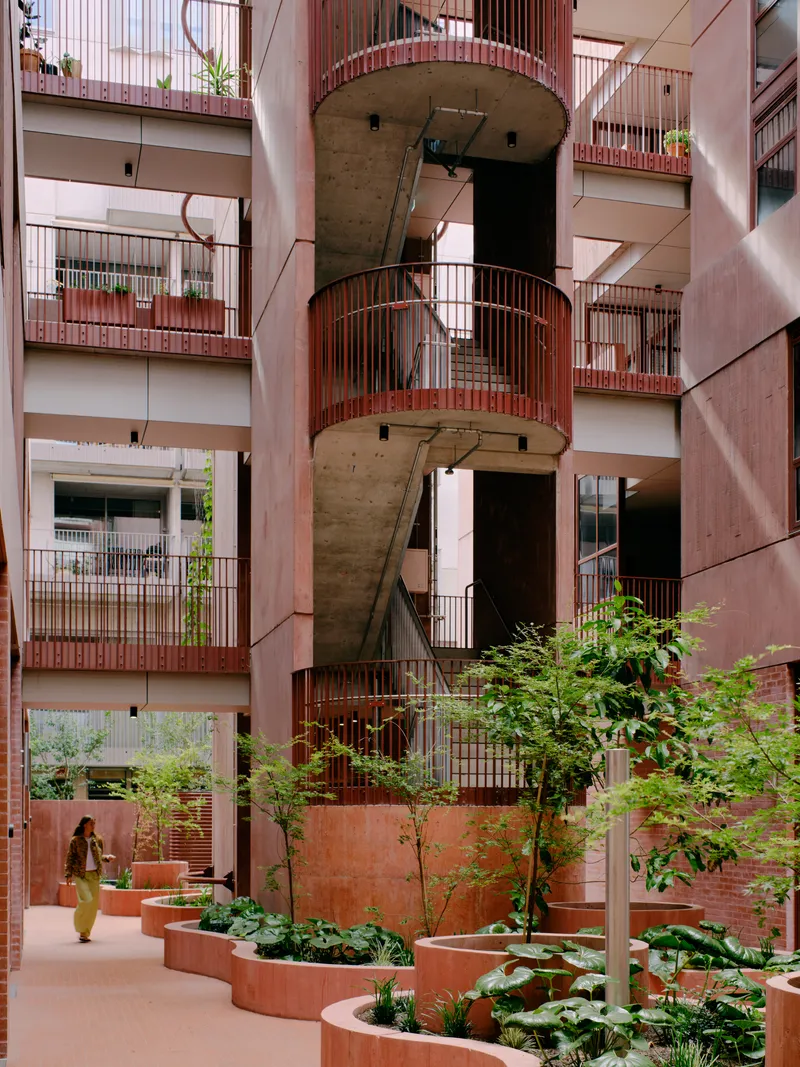 Central courtyard with concrete spiral stair wrapped by pink metal railings and planted beds below
