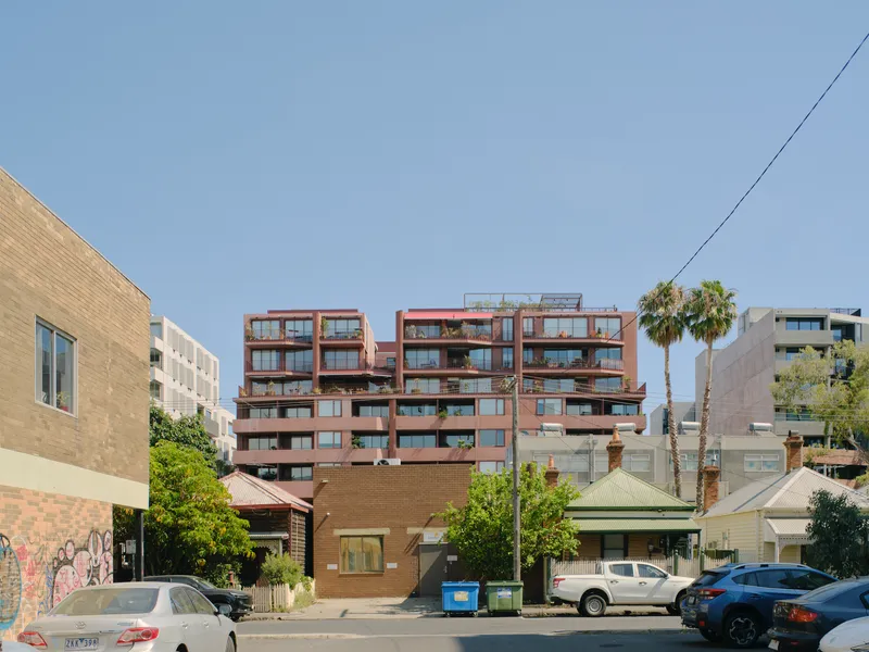 Facade of terraced apartment building with staggered balconies framed by palm trees and power lines