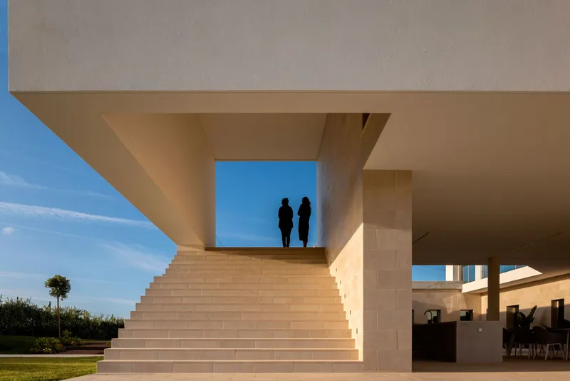Stone staircase rising beneath the cantilevered upper volume with two silhouetted figures