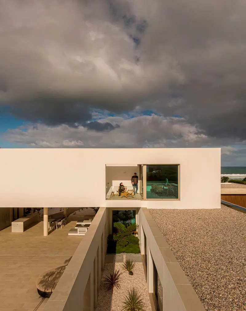 Upper terrace with figures on gravel roof and planted courtyard below under storm clouds