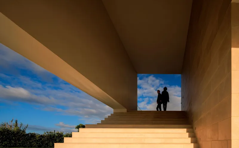 Stone staircase framing two figures silhouetted against blue sky with scattered clouds