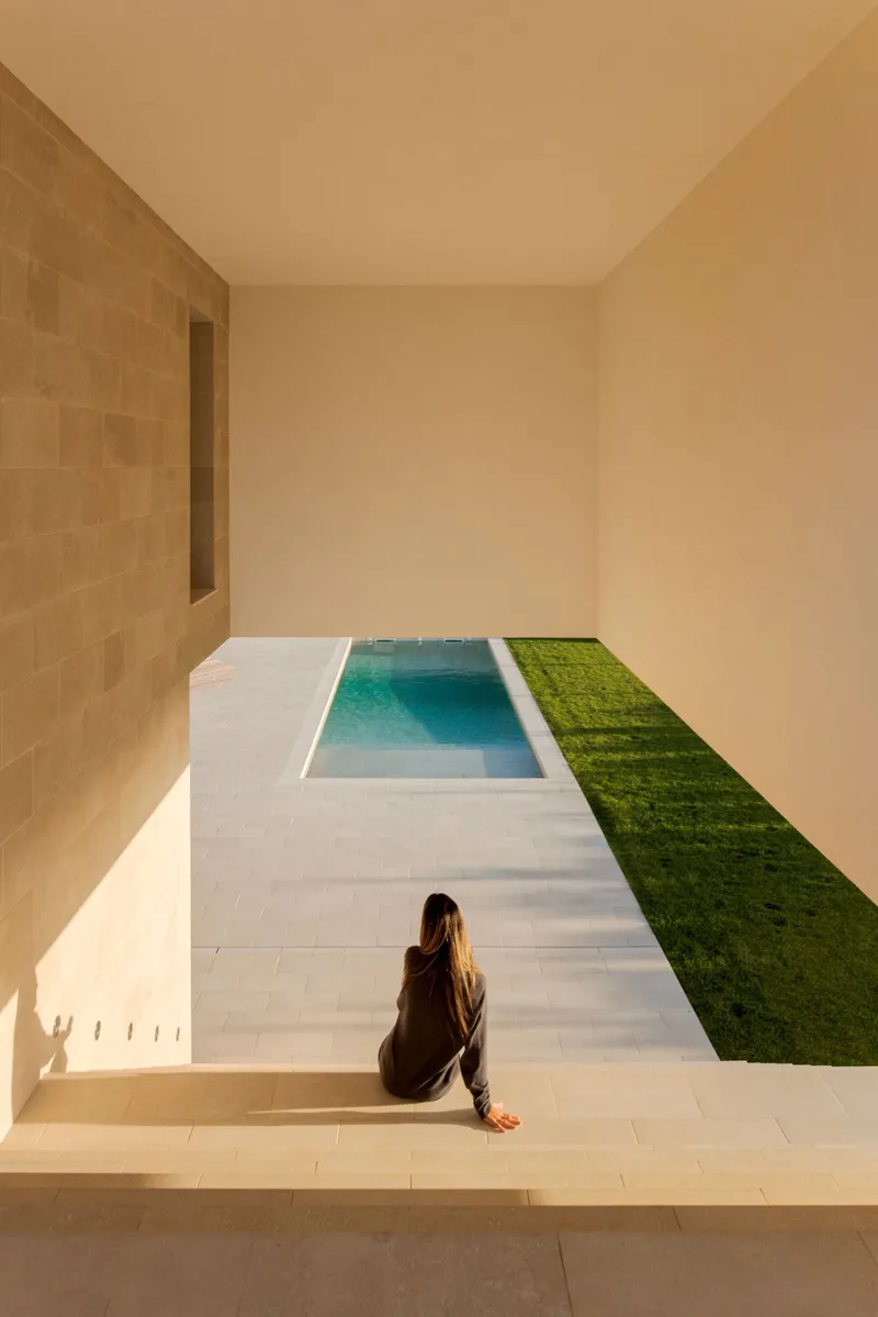 Courtyard with rectangular pool bordered by white paving and grass strip with seated figure