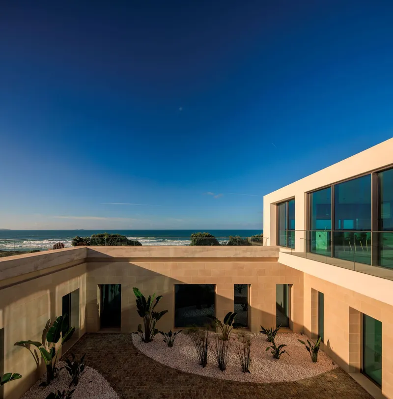 Upper terrace with planted courtyard and glazed facade overlooking the ocean under clear blue sky