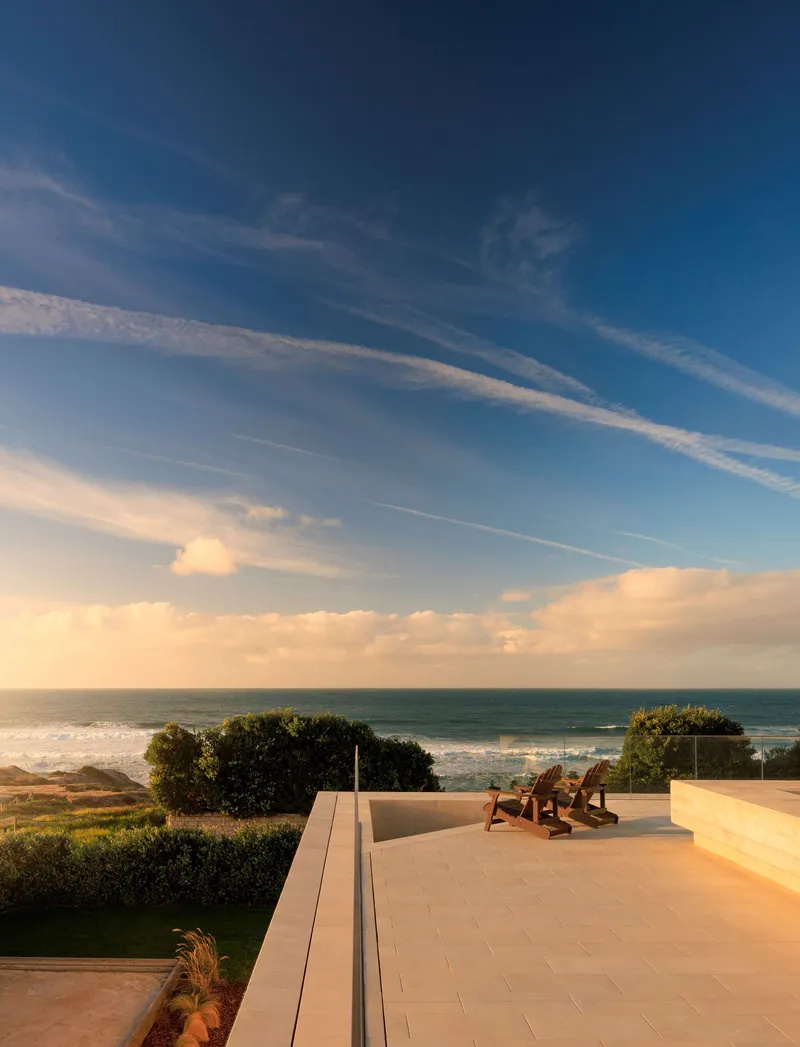 Rooftop terrace with wooden loungers facing the sea at sunset with wispy clouds above