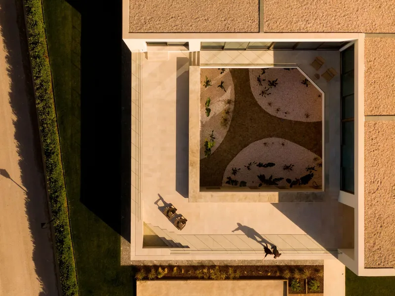 Aerial view of a courtyard with curved planted beds and three people casting long shadows in afternoon light