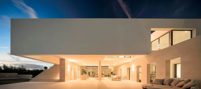 Exterior terrace with cantilevered volume above illuminated open-air living space at dusk