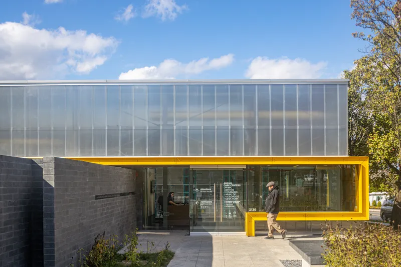 Yellow steel-framed entrance canopy with person walking past beneath polycarbonate upper level