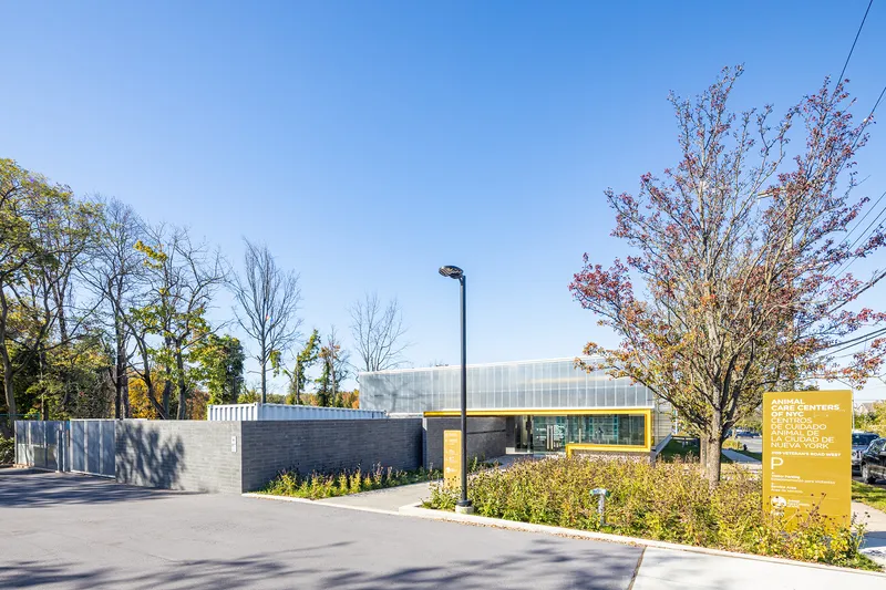 Site view showing planted beds, parking area and translucent roof volume among autumn trees