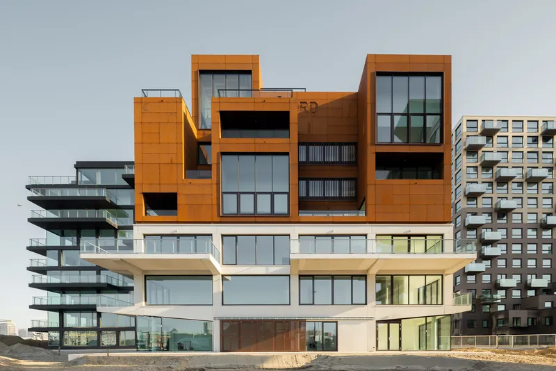 Street-level view of the articulated base with cor-ten steel volumes above white ground floor units