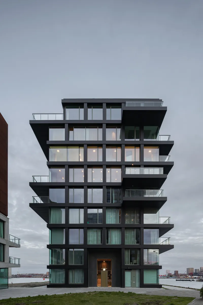 Tower facade with staggered black balconies and floor-to-ceiling glazing photographed at dusk