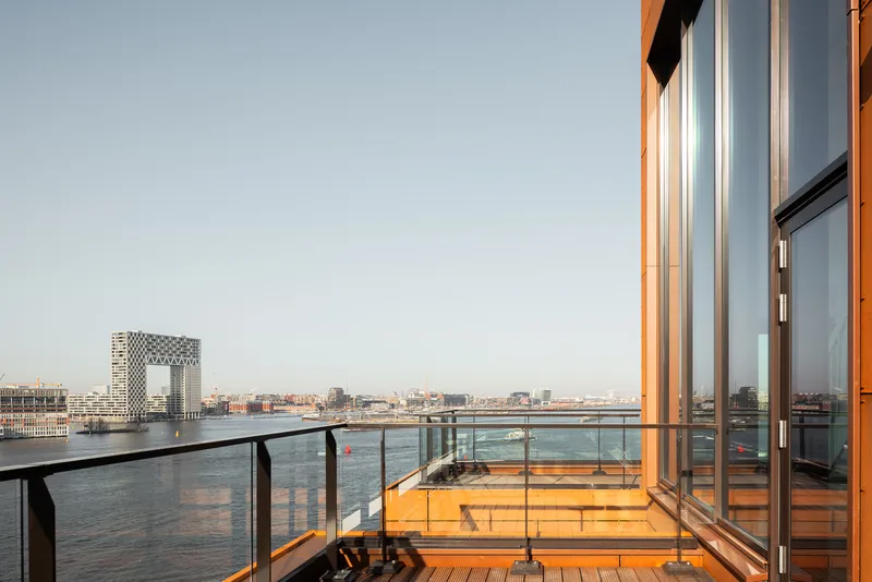 Rooftop terrace with timber decking and glass balustrade facing the waterfront at dusk