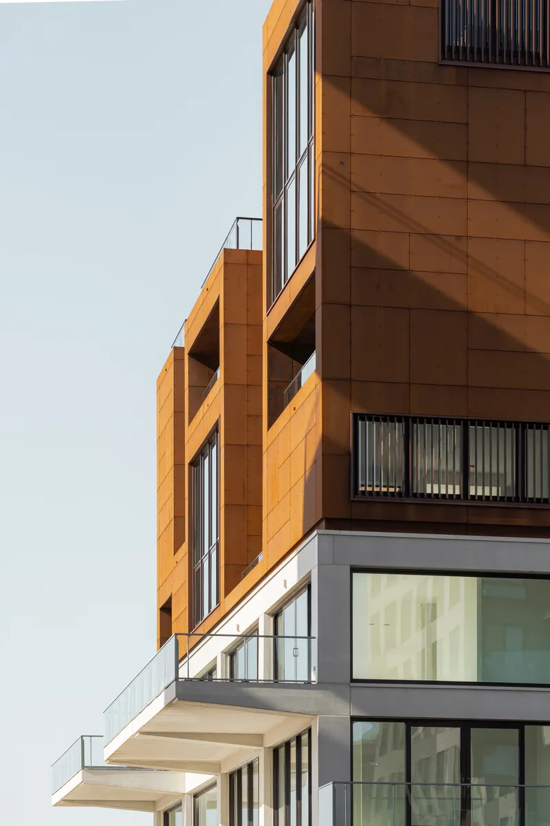 Stacked balconies with cantilevered orange panels and glass railings against a clear sky