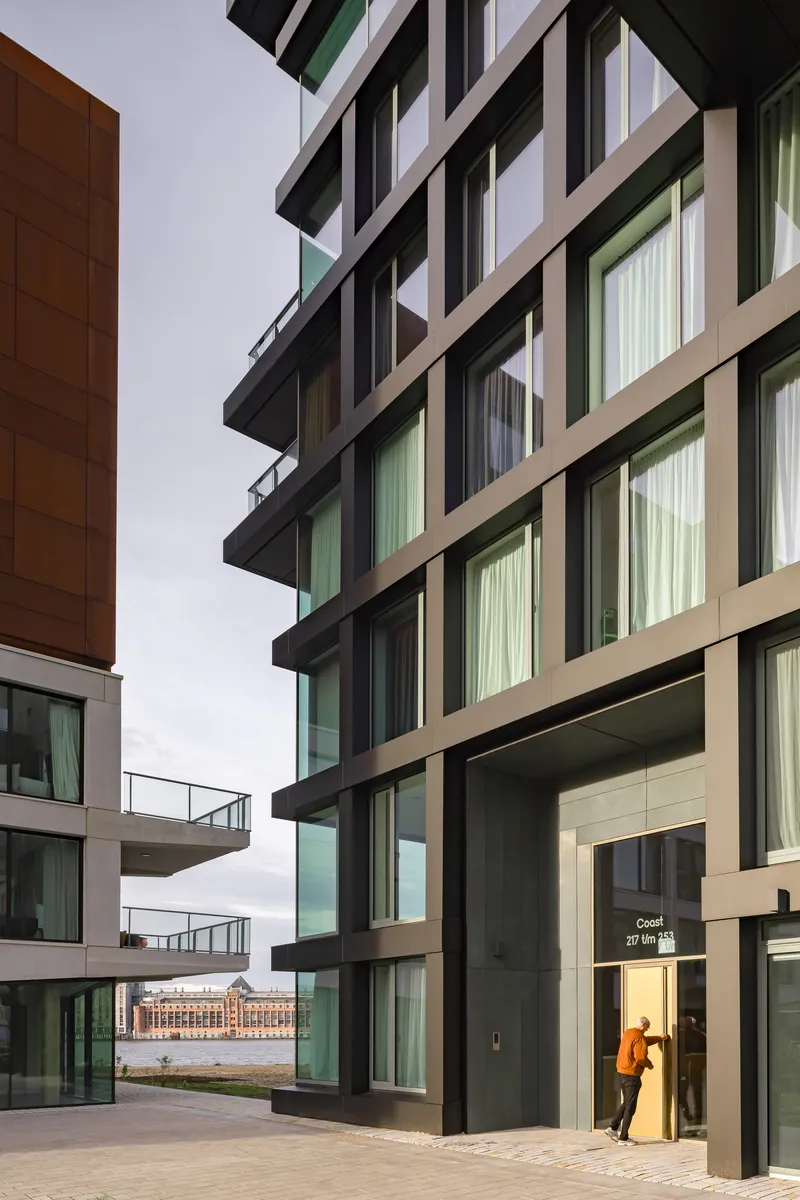 Ground-level view of the dark framed facade with projecting balconies and a person entering the lobby