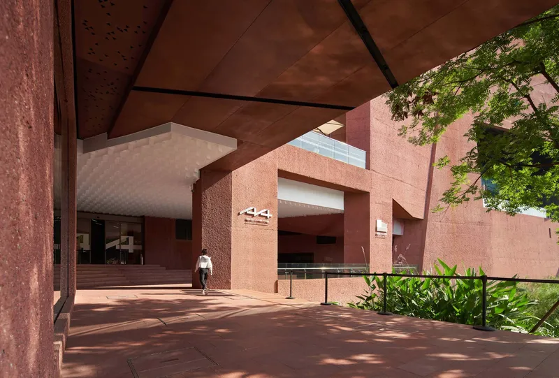 Covered entrance courtyard with red stone paving and textured pink walls framed by tropical foliage