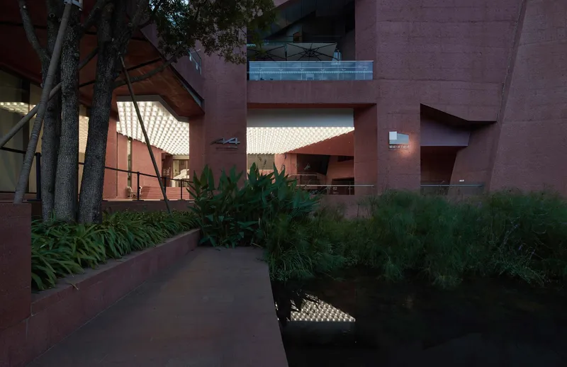 Courtyard view with planted beds and water feature beneath illuminated waffled ceiling canopies at dusk