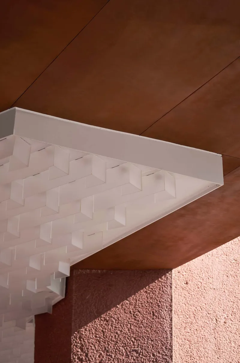 Detail of white three-dimensional coffered ceiling panel meeting a corten steel soffit and pink textured wall